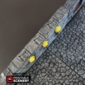 May include: A close-up of a gray stone wall with a cobblestone path. The wall has a textured surface and is painted with a light gray color. The path is made of small, irregular stones and is painted with a dark gray color. There are four yellow lights on the wall, illuminating the path.