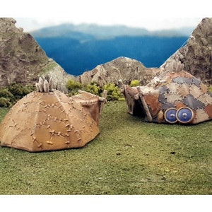 Puede incluir: Dos tiendas de campa&ntilde;a en miniatura, hechas a mano, de cuero marr&oacute;n con detalles cosidos. Una tienda tiene dos ojos circulares azules. Ambas tiendas est&aacute;n sobre una superficie de hierba verde.