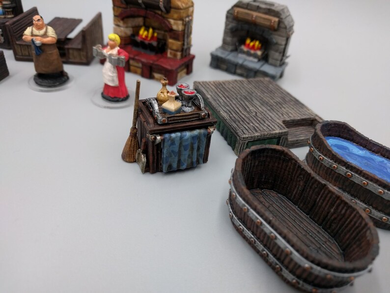 May include: A miniature wooden bar trolley with a blue cloth draped over the side. The trolley is filled with miniature bottles, glasses, and a broom. The trolley is on a white surface.