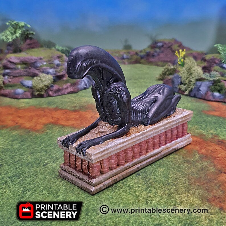 Pode incluir: Uma figura negra de Xenomorfo em pose de esfinge, repousando sobre uma base retangular com um design detalhado. A base tem um esquema de cores marrom-avermelhado e bege. A figura est&aacute; situada em um cen&aacute;rio de paisagem verde.