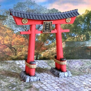 May include: A red and black miniature torii gate with a gold plaque that reads "松" in Japanese. The gate is set on a stone base and surrounded by a cobblestone path.