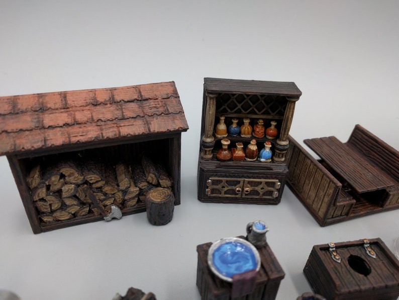 May include: A set of miniature wooden furniture pieces for tabletop gaming, including a wood-burning stove, a cabinet with shelves, a bench, a table with a basin, and a small chest.