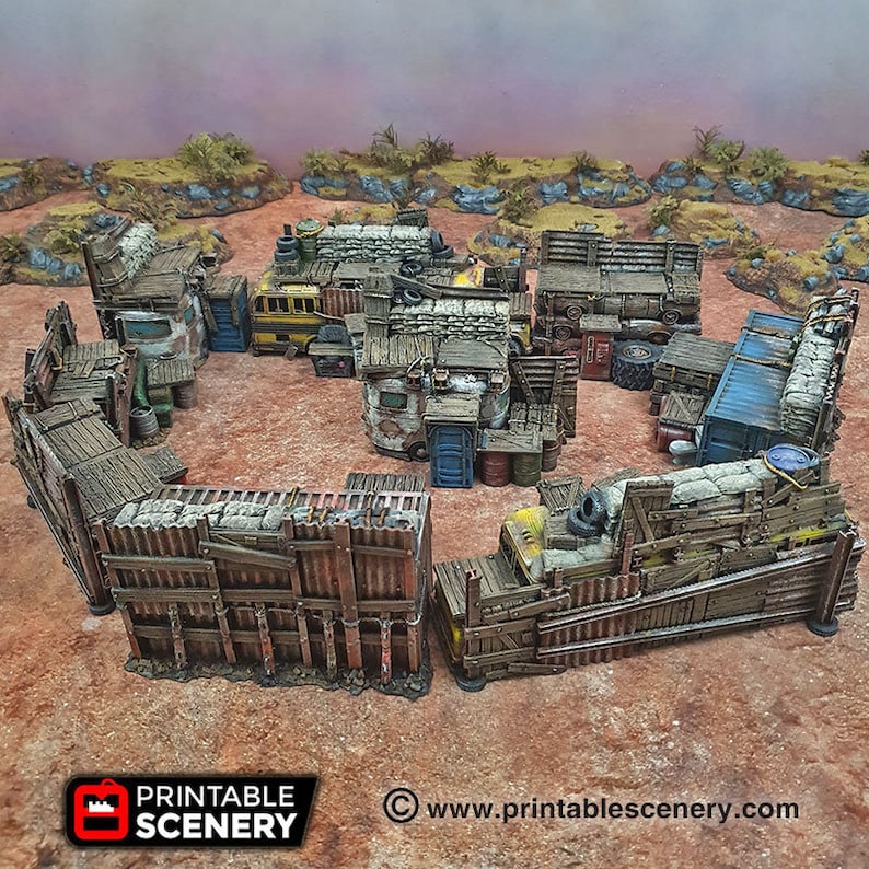 May include: A model of a post-apocalyptic settlement made from scrap metal and wood. The settlement is surrounded by a fence made of corrugated metal and wood. There are several buildings inside the settlement, including a bus, a trailer, and a shipping container. The settlement is set on a sandy surface.
