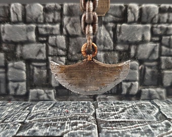 Pode incluir: Uma lâmina de metal de cor marrom enferrujada em forma de crescente pendura em uma corrente. A lâmina está presa a um anel na parte superior da corrente. A lâmina está pendurada na frente de uma parede de pedra.