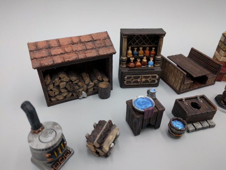 May include: A collection of miniature wooden furniture and accessories for tabletop gaming, including a wood-burning stove, a woodpile, a small table with a blue bowl, a wooden bench, a small wooden shed, and a cabinet with shelves filled with potion bottles.