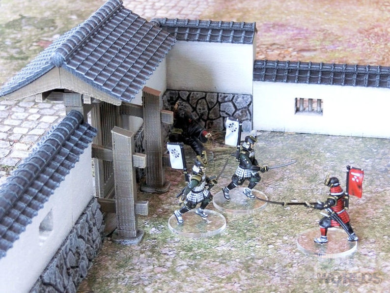 May include: A miniature scene depicting a battle between samurai warriors. The scene features a Japanese-style gate, a wall, and several figures in traditional samurai armor. The figures are holding swords and are engaged in combat. The scene is painted in a realistic style and is suitable for use in tabletop wargaming.