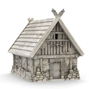 Op de afbeelding: Een klein, wit, houten huis met een zadeldak en een stenen fundering. Het dak heeft een decoratieve houten carving op de top. Het huis heeft een enkele deur en een klein raam.