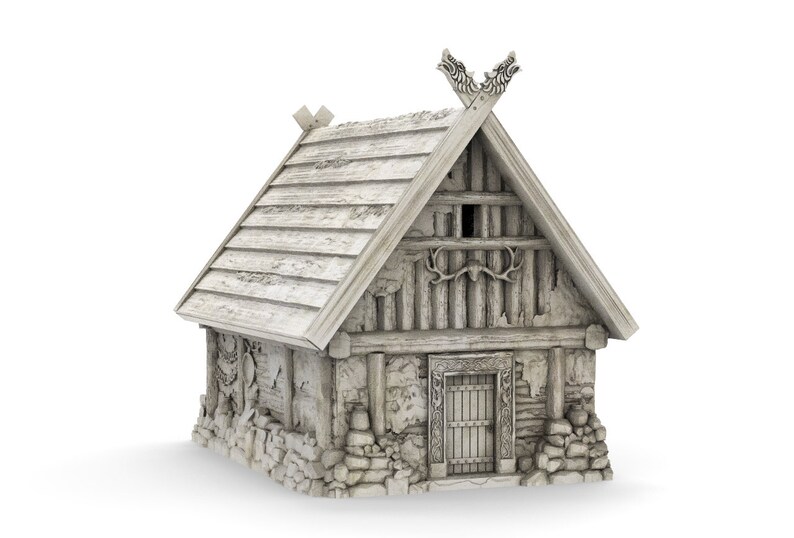 Op de afbeelding: Een klein, wit, houten huis met een zadeldak en een stenen fundering. Het dak heeft een decoratieve houten carving op de top. Het huis heeft een enkele deur en een klein raam.