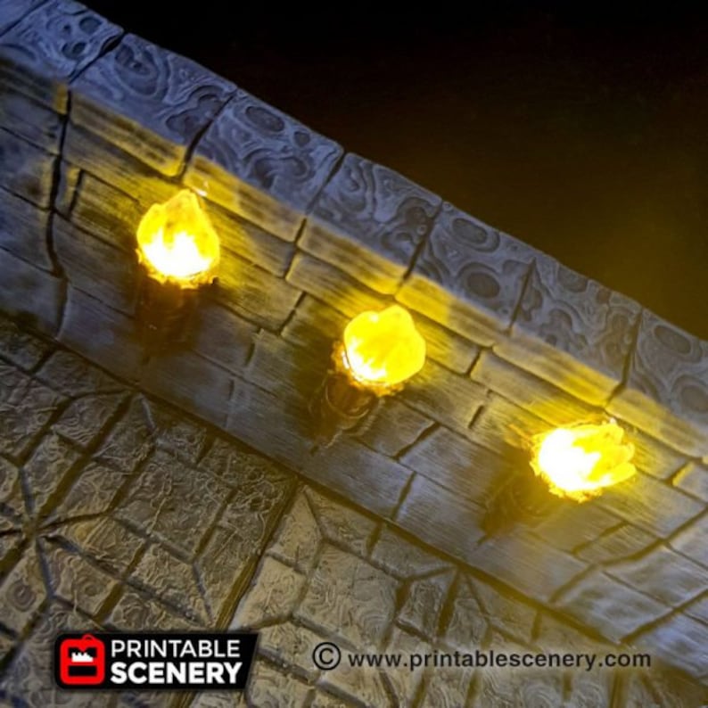May include: Three lit torches mounted on a stone wall. The torches are made of a light brown material and have a yellow flame. The wall is made of a dark gray stone with a rough texture. The text "www.printablescenery.com" is visible in the lower right corner of the image.