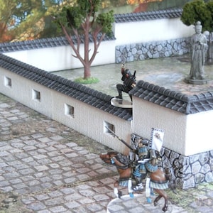 May include: A miniature scene depicting a Japanese garden with a white wall, a stone path, and a small tree. Two figures, one in black and one in armor, are positioned near the wall. The scene is designed for tabletop gaming.