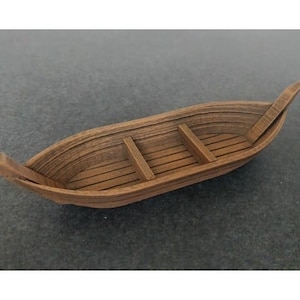 May include: A wooden boat with a pointed bow and stern, featuring three rows of seats. The boat is made of light brown wood and has a natural finish.
