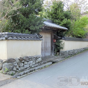 May include: A traditional Japanese style home with a stone wall and a wooden gate. The wall is made of stacked stones and is painted white. The gate is made of wood and has a dark brown finish. The gate is closed and has a small mailbox on the right side.