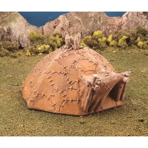 Puede incluir: Un peque&ntilde;o modelo de caba&ntilde;a de madera y paja, de color marr&oacute;n y beige. La caba&ntilde;a est&aacute; hecha de un material que parece cuero o tela, y tiene una peque&ntilde;a abertura en la parte delantera.