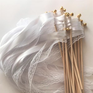 May include: A bundle of white satin and lace ribbon wands with gold bells attached to the ends. The wands are made of wooden dowels.