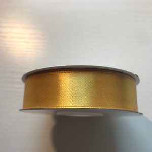May include: A spool of gold satin ribbon. The ribbon is wound around a white cardboard spool.