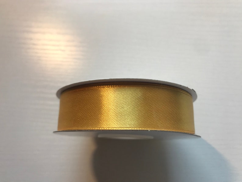 May include: A spool of gold satin ribbon. The ribbon is wound around a white cardboard spool.
