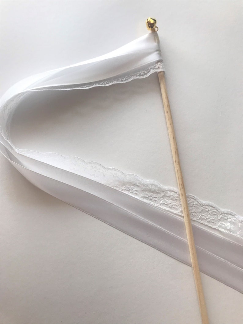 May include: White satin ribbon wand with a gold bell at the top. The ribbon has a lace trim and is attached to a wooden stick.