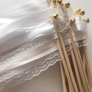 May include: A set of white satin ribbon wands with lace trim and gold bells. The wands are tied together and have wooden sticks.