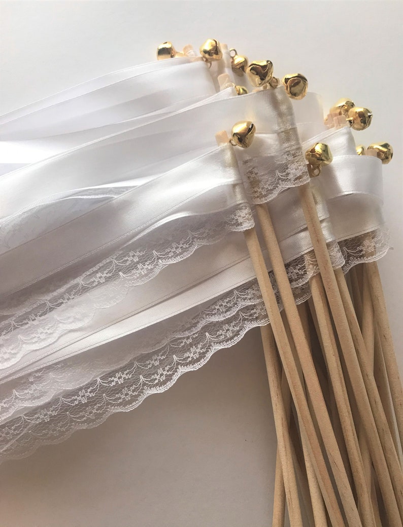 May include: A set of white satin ribbon wands with lace trim and gold bells. The wands are tied together and have wooden sticks.