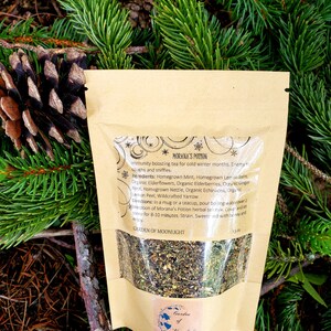 May include: A brown paper bag with a white label that says "Morana's Potion" and "Garden of Moonlight". The label also lists the ingredients for an immunity boosting tea, including mint, lemon balm, elderflowers, elderberries, ginger root, nettle, echinacea, lemon peel, and yarrow.