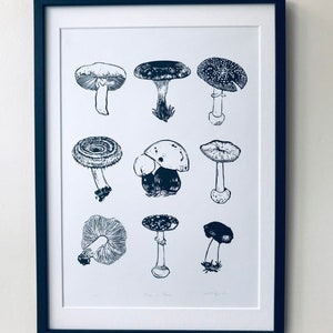 May include: A black and white print of various mushroom illustrations. The print is framed in a black frame and is hanging on a white wall.