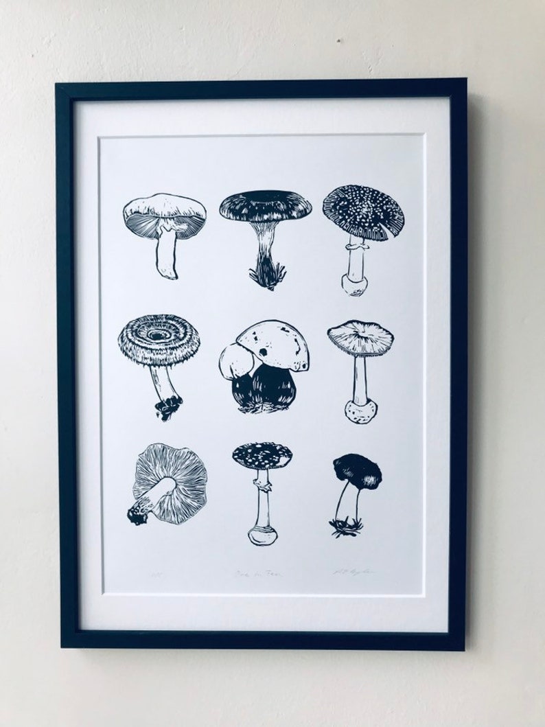 May include: A black and white print of various mushroom illustrations. The print is framed in a black frame and is hanging on a white wall.