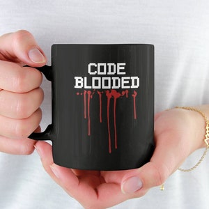 Puede incluir: Taza de café negra con un diseño blanco que dice "CODE BLOODED" con sangre roja goteando.
