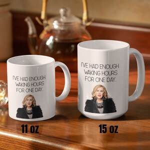 May include: Two white ceramic mugs with the text "I'VE HAD ENOUGH WAKING HOURS FOR ONE DAY." and an illustration of a woman. One mug is labeled 11 oz, the other 15 oz. A teapot is in the background.