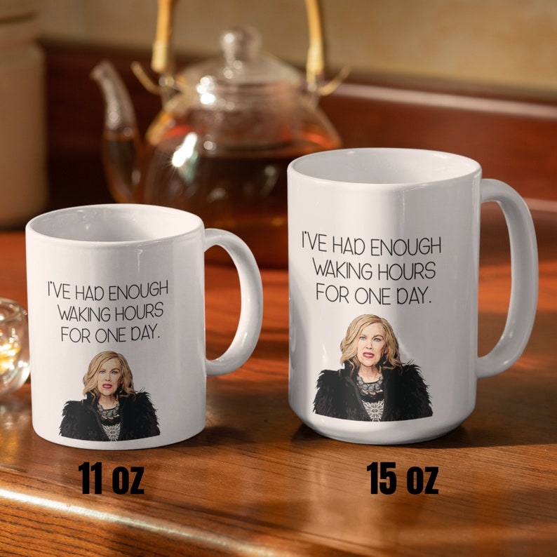 May include: Two white ceramic mugs with the text "I'VE HAD ENOUGH WAKING HOURS FOR ONE DAY." and an illustration of a woman. One mug is labeled 11 oz, the other 15 oz. A teapot is in the background.