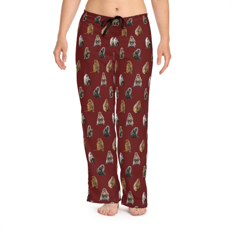 May include: Burgundy pajama pants with a repeating pattern of various colored monkeys. The pants have a drawstring waist and a relaxed fit. The monkeys are in shades of brown, gray, and tan.
