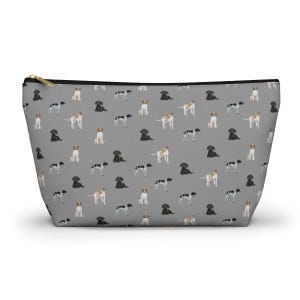 Puede incluir: Una bolsa de cremallera gris con un patrón repetido de perros negros, blancos y marrones. Los perros están todos de pie y mirando en diferentes direcciones.
