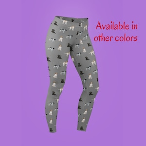 Könnte beinhalten: Graue Leggings mit einem sich wiederholenden Muster aus braunen, schwarzen und weißen Hunden. Der Text "Erhältlich in anderen Farben" ist in Rot oben rechts im Bild.
