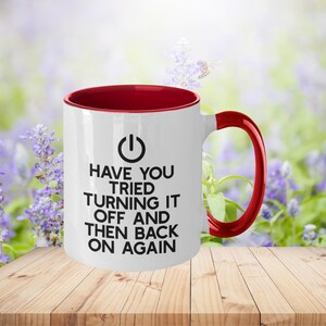 May include: White ceramic mug with a red rim and handle. The mug has a black power button symbol and the text "Have you tried turning it off and then back on again".
