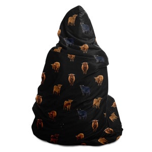 May include: Black hooded blanket with a repeating pattern of brown and black Highland cattle. The blanket is made of soft, plush fabric and has a large hood.