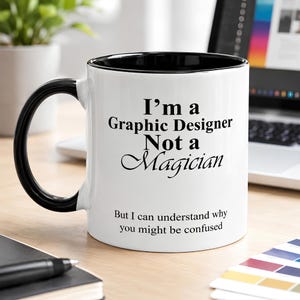 Black accent ceramic mug featuring the phrase “I’m A Graphic Designer, Not A Magician” in a clean creative workspace setting.