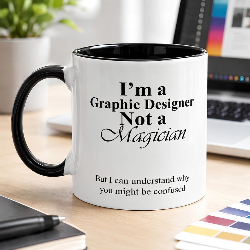 Black accent ceramic mug featuring the phrase “I’m A Graphic Designer, Not A Magician” in a clean creative workspace setting.