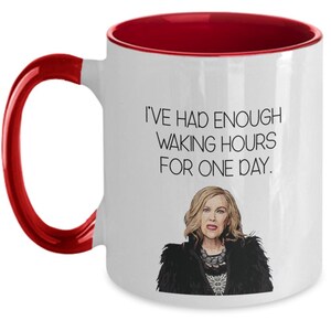 May include: White ceramic mug with a red interior and handle. The mug features the text "I'VE HAD ENOUGH WAKING HOURS FOR ONE DAY" and an illustration of a woman with blonde hair and a black jacket. A humorous gift.