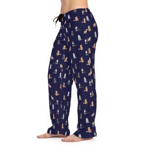 Puede incluir: Pantalón de pijama azul marino con un patrón repetido de gatos coloridos. El pantalón tiene una cintura con cordón y un ajuste holgado.