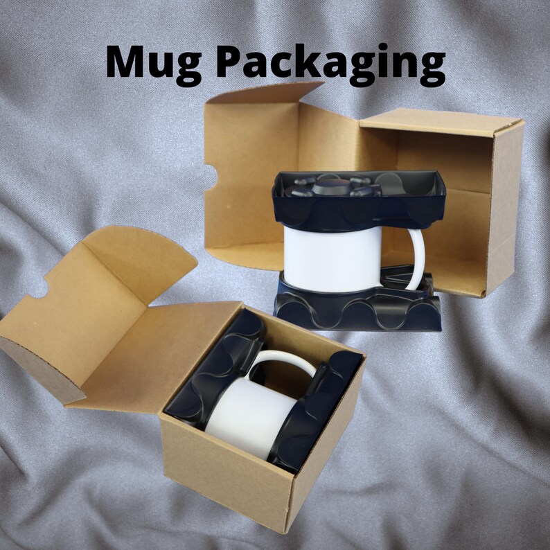 以下が含まれることがあります： ふたが開いた茶色の段ボール箱が2つあり、それぞれに黒い取っ手付きの白いセラミックマグカップが入っています。マグカップは黒いフォームインサートに収められています。画像の上部に「Mug Packaging」というテキストが印刷されています。