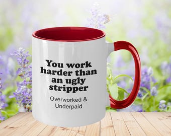 May include: White ceramic mug with a red rim and handle. The mug has black text that reads "You work harder than an ugly stripper Overworked & Underpaid".