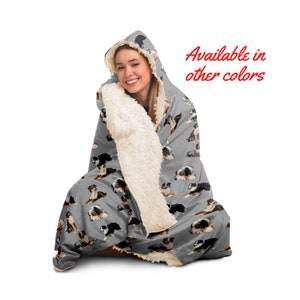 May include: A gray hooded blanket with a white sherpa lining features a repeating pattern of Australian Shepherd dogs. The text "Available in other colors" is displayed in red.