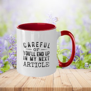 May include: White ceramic mug with a red rim and handle. The mug has black text that reads "Careful or you'll end up in my next article."