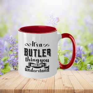 Puede incluir: Taza de cerámica blanca con borde y asa rojos. La taza tiene texto negro que dice "It's a Butler thing you wouldn't understand".