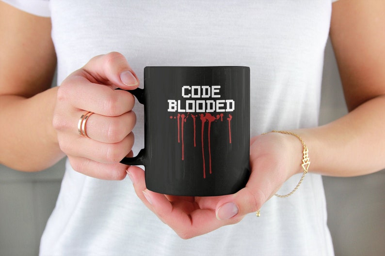 以下が含まれることがあります： 白い「CODE BLOODED」の文字と赤い血が滴るデザインが施された黒いコーヒーカップ。