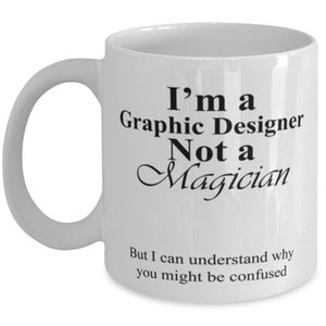 May include: White ceramic mug with a curved handle. The mug features black text that reads "I'm a Graphic Designer Not a Magician" and "But I can understand why you might be confused."
