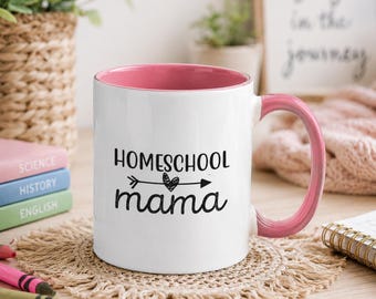 Puede incluir: Una taza de cerámica blanca con interior y asa de color rosa. La parte frontal presenta el texto negro "HOMESCHOOL mama" con un pequeño gráfico de flecha que contiene un corazón en el centro, situado entre las dos palabras.