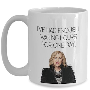 May include: White ceramic mug with a black handle featuring the text "I'VE HAD ENOUGH WAKING HOURS FOR ONE DAY." Below the text is a cartoon image of a woman with blonde hair wearing a black jacket.