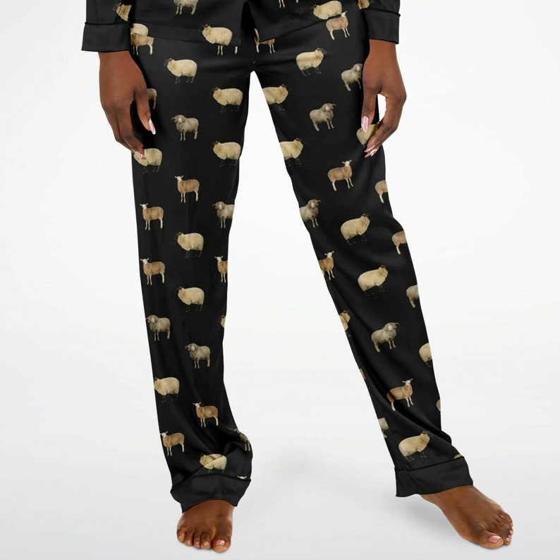 以下が含まれることがあります： 茶色と白の羊が繰り返し描かれた黒いパジャマパンツ