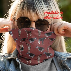 May include: A red face mask with a pattern of Okapi, a type of African mammal, printed on it. The mask is being worn by a person with blonde hair and sunglasses. The text "Available in other colors" is visible in the upper right corner of the image.