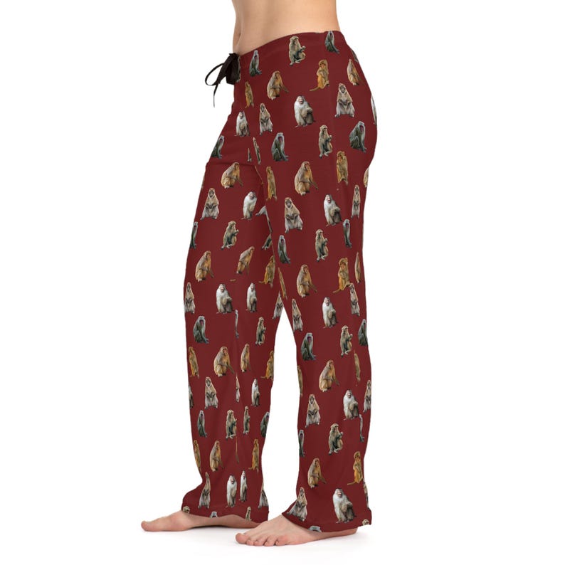 May include: Burgundy pajama pants featuring a repeating pattern of various monkey illustrations. The pants have a drawstring waist and a relaxed fit. The monkeys are depicted in shades of brown, gray, and white.